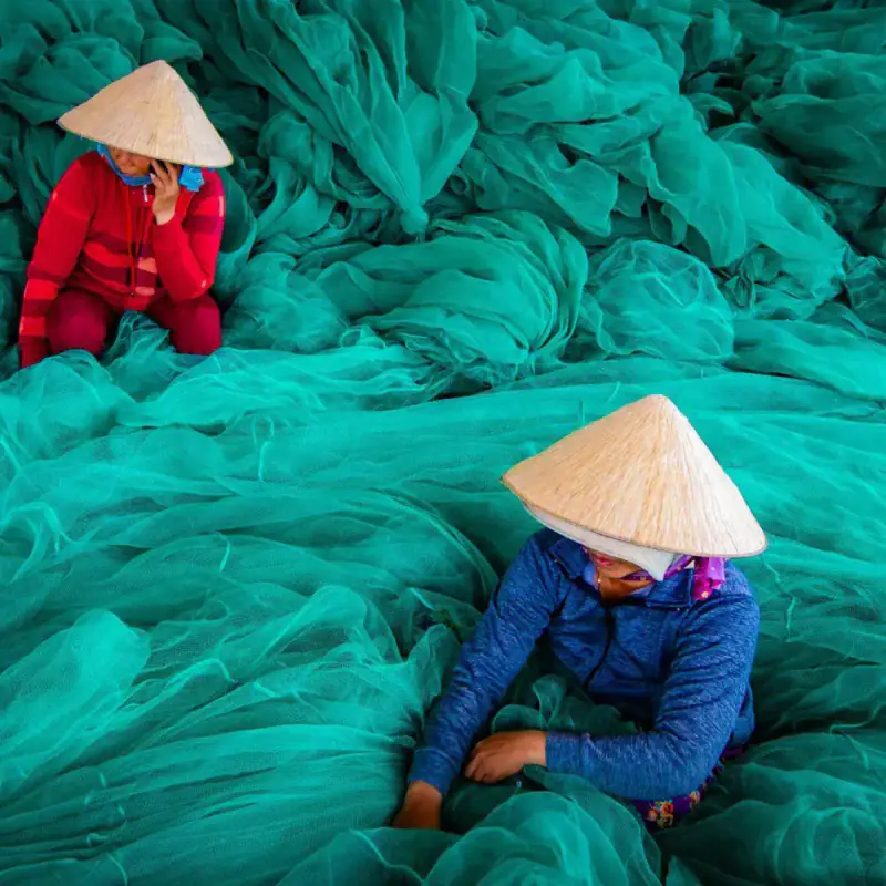 Two workers in conical hats among fishing nets